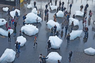 Visitors interact with blocks of melting ice from an exhibit outside Tate Modern in central London to illustrate A measure of reality