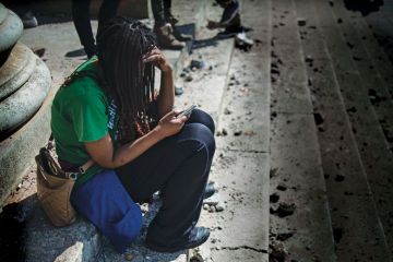 A woman looks at her phone  as she sits on steps of a University