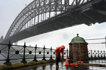 A construction worker sweeps away water while it rains next to the Harbour Bridge in Sydney to illustrate Shortened work rights ‘complicate’ skills drive