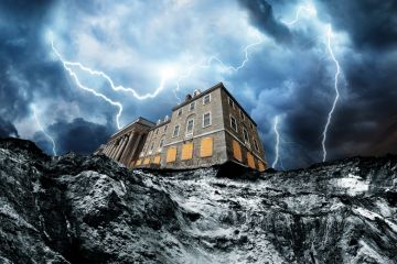 A house partially hangs over a cliff edge following rapid coastal erosion with lightening to illustrate What would happen if a  UK university went bankrupt?