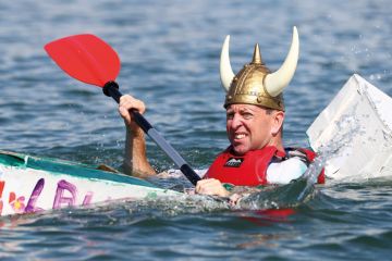 Person wearing viking hat in a cardboard boat sinking at a boat Regatta to illustrate the Danish humanities courses pressed on contact hours as funding cut