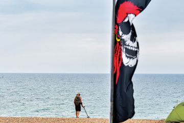 A man walks along Brighton Beach using a metal detector to illustrate Programs are not detecting AI text. Is regulation needed to halt cheats?