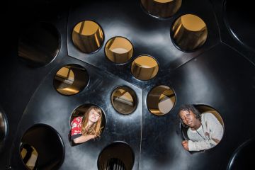 Two people looking inside holes in an immersive art installation in London, UK_to illustrate Academics urged to fill policy void at heart of new UK government
