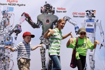 Children pose in front of a promotional poster during the finals of the DARPA Robotics Challenge to illustrate Canada joining the rush to create a Darpa