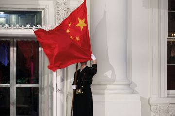 A military honor guard holds the Chinese flag in front of the White House in Washington which has blown over his face to illustrate Republicans target universities over China and political research