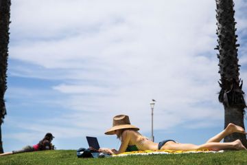 Person sunbathing in a bikini with her laptop 