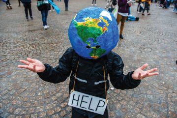 A man with an earth ball on his head and help sign makes hand gesture