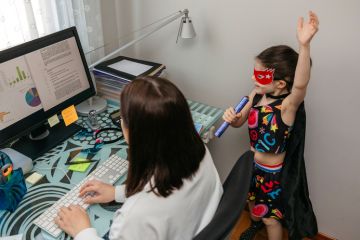 Woman working from home with her daughter singing by her side