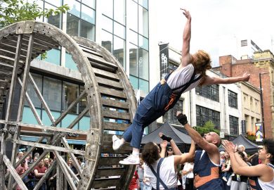  A performer on a rolling wooden wheel falls backwards, knowing that her team members will catch her