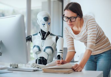 AI robot sat at a computer, while a woman in glasses sits next to pointing at a paper