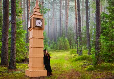 Graduate leaning on model of Big Ben in forest