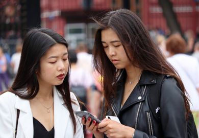 Two girls look at smartphone standing on Manezh square in the Moscow