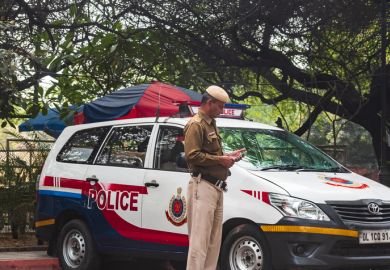 Delhi, India: A policeman in front of a red and white mini van patrolling the state border of the Delhi, state.