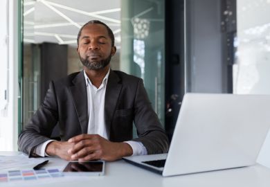 An academic closes his eyes at his desk, symbolising self-care