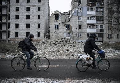 Two people cycle past bombed buildings in Ukraine