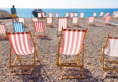 Man looking out to sea with empty deckchairs along the beach in Devon, UK to illustrate English universities battle rising tide of student no-shows
