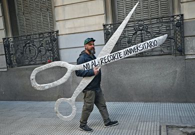 A demonstrator holds a giant scissors that read in Spanish "No to the University Cuts" to illustrate Argentine academics flee Milei’s austerity crusade