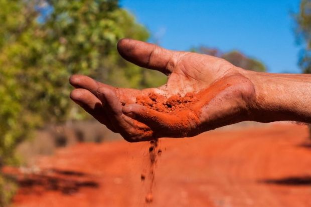 Red Australian earth slips through an Indigenous Australian’s fingers