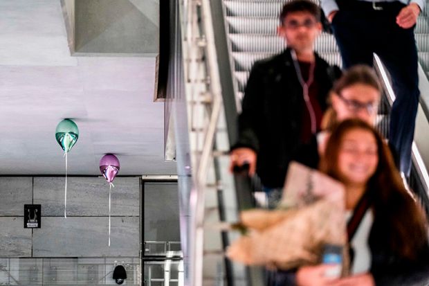 People travelling down escalator with balloons touching ceiling by artist Jeppe Hein. To illustrate cash-strapped universities deciding against raising fees for current students.