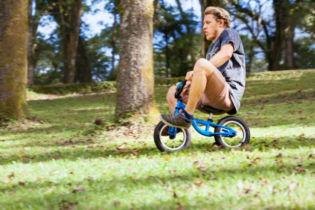 A man rides a child's bicycle, illustrating the need for growth