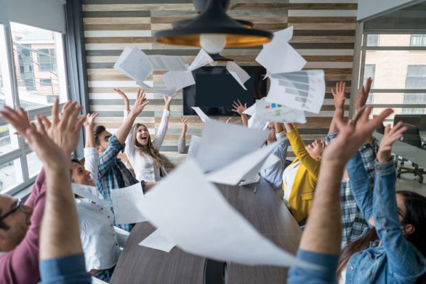 Boardroom of people celebrating and throwing papers in air