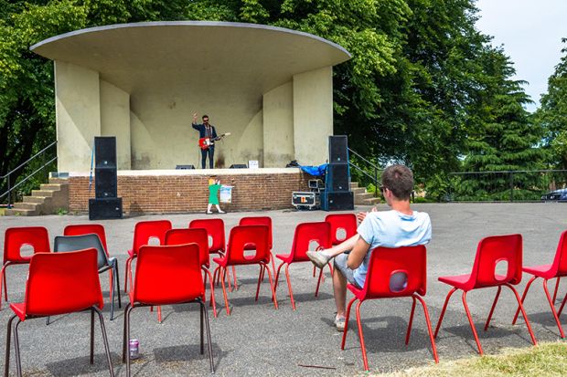 One person with empty seats watching a guitarist on stage, illustrating that the number of international students enrolling in the English higher education sector has fallen by more than a tenth this year