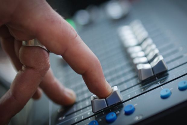 A finger slides down a fader on a mixing desk, illustrating the fading out of music scholarship