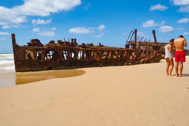 Fraser Island Australia; Two tourists on beach by Maheno shipwreck rusting away on beach