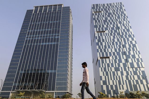 A pedestrian walks past 2 buildings in Gujarat International Finance Tec-City (GIFT City), Gujarat, India