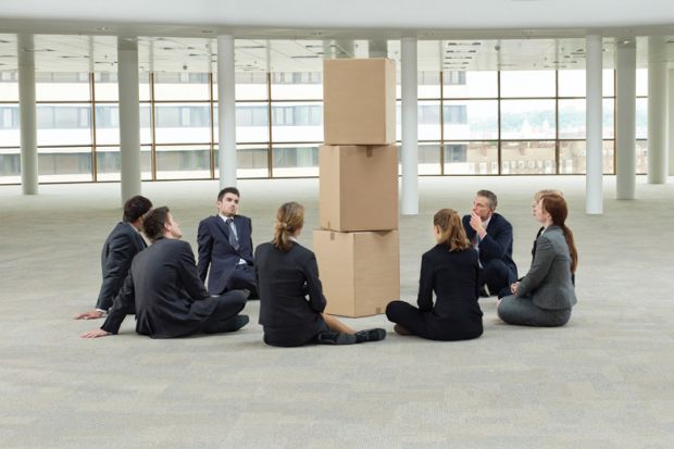 Group of businesspeople sat around pile of cardboard boxes