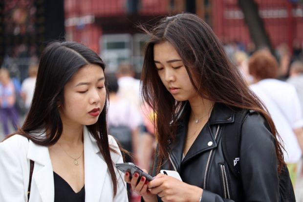 Two girls look at smartphone standing on Manezh square in the Moscow