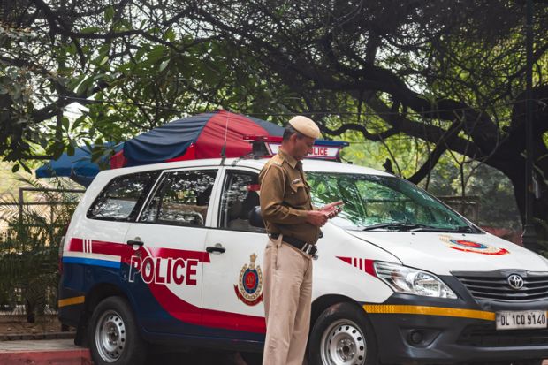 Delhi, India: A policeman in front of a red and white mini van patrolling the state border of the Delhi, state.
