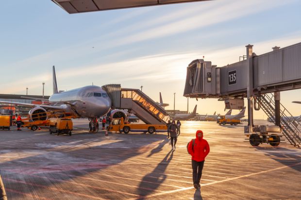 Front view big modern passenger aircraft approach boarding with stairs vehicle against airport building morning evening warm sun.