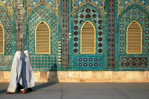 Two women wearing white burqas (burkas) walk past the Blue Mosque in Mazar-i-Sharif, Balkh Province, Afghanistan.