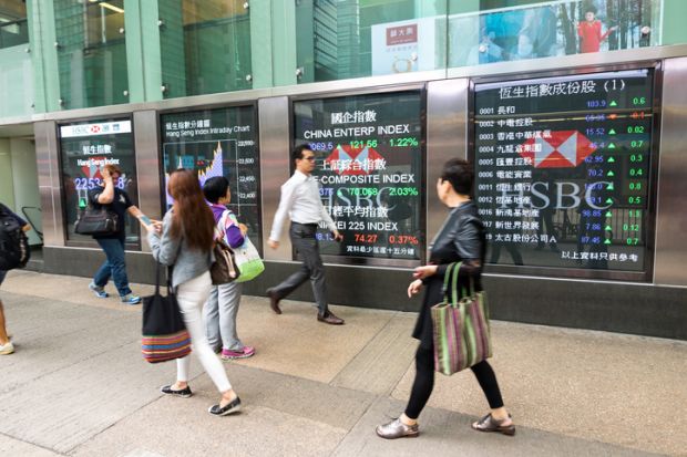 Pedestrians walk past a financial display board in Mong Kok, Kowloon, Hong Kong, China.