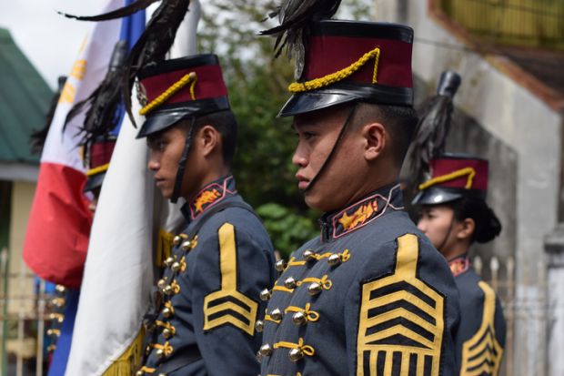 Male College military cadet on standing formation holding national flag.