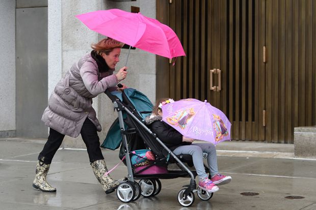 A mother pushing a child in a pushchair with the child concealed by an umbrella