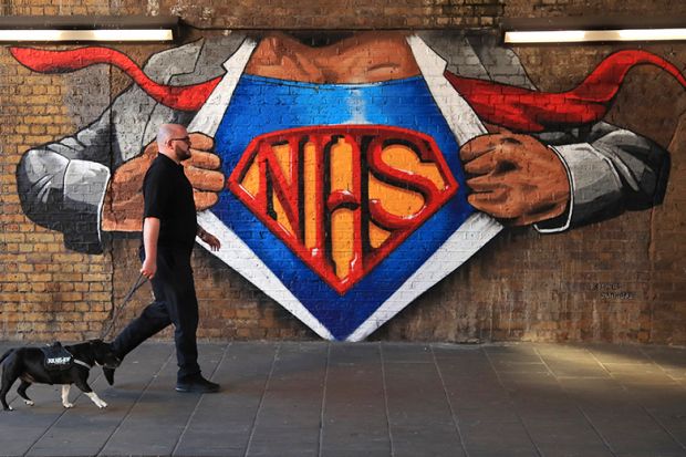 A man and a dog walk past an NHS mural showing superman, illustrating that a new applied research centre focused on NHS transformation could be created.