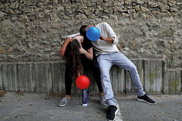 Two young people inhale nitrous oxide from balloons