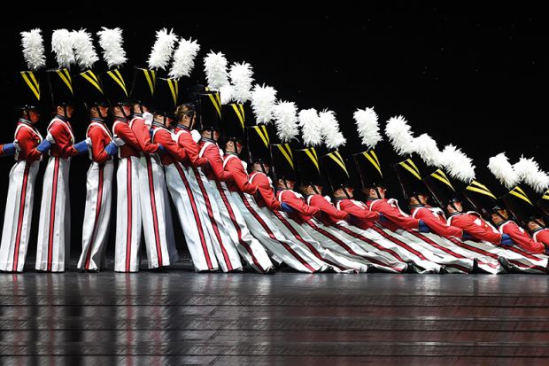 People dressed as soldiers falling like dominoes. To illustrate the "domino effect" of US colleges embracing institutional neutrality.