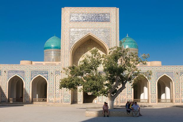 People sitting in the shade of a tree near a mosque, Uzbekistan. To illustrate branch campuses being set up in the country.