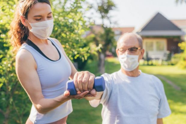 A physiotherapist helps an old man exercise