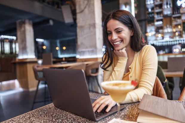 A woman drinks a cocktail and works on her laptop, symbolising residential courses