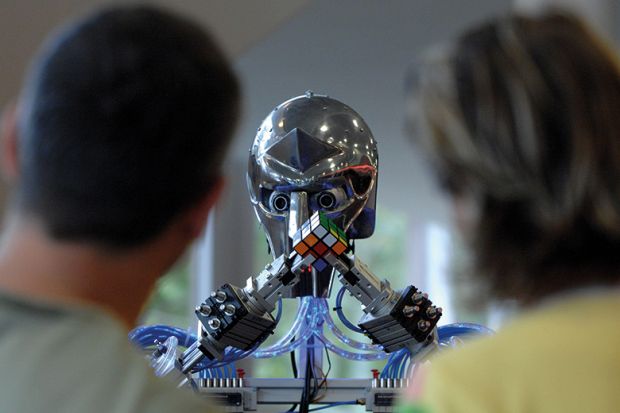 People watch a robot grapple with a Rubik's Cube