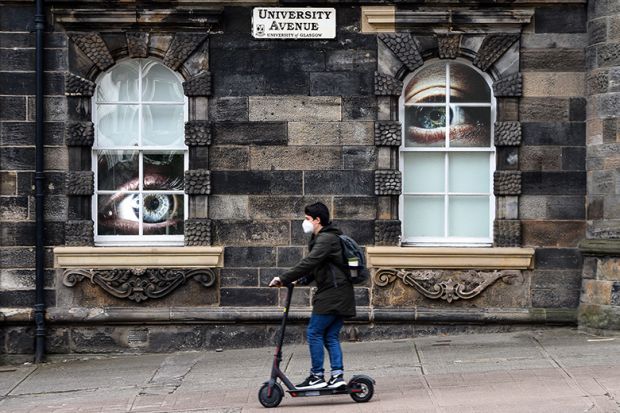 Student on a scooter on campus at the University of Glasgow, with large eyes looking at him through windows. To illustrate the university being placed on a student visa sponsorship “action plan” by the Home Office