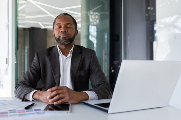 An academic closes his eyes at his desk, symbolising self-care