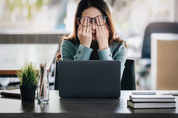 Woman looking stressed at a laptop with her hands over her eyes