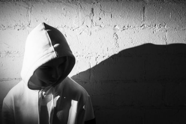Teenage boy with his hood up against a white brick wall