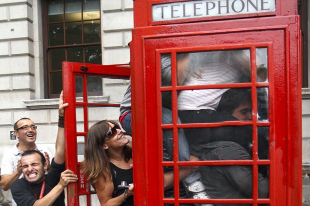 People squeezing in to a telephone box, illustrating class size increases.