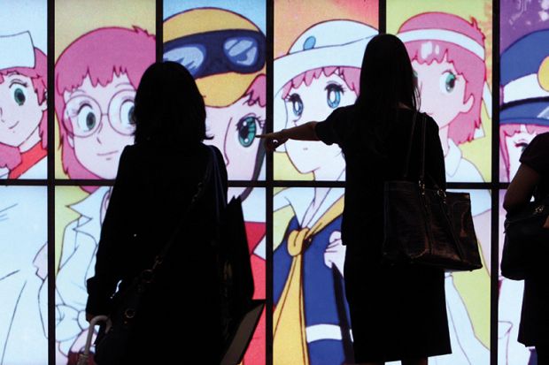 People silhouetted against a screen showing Japanese anime 